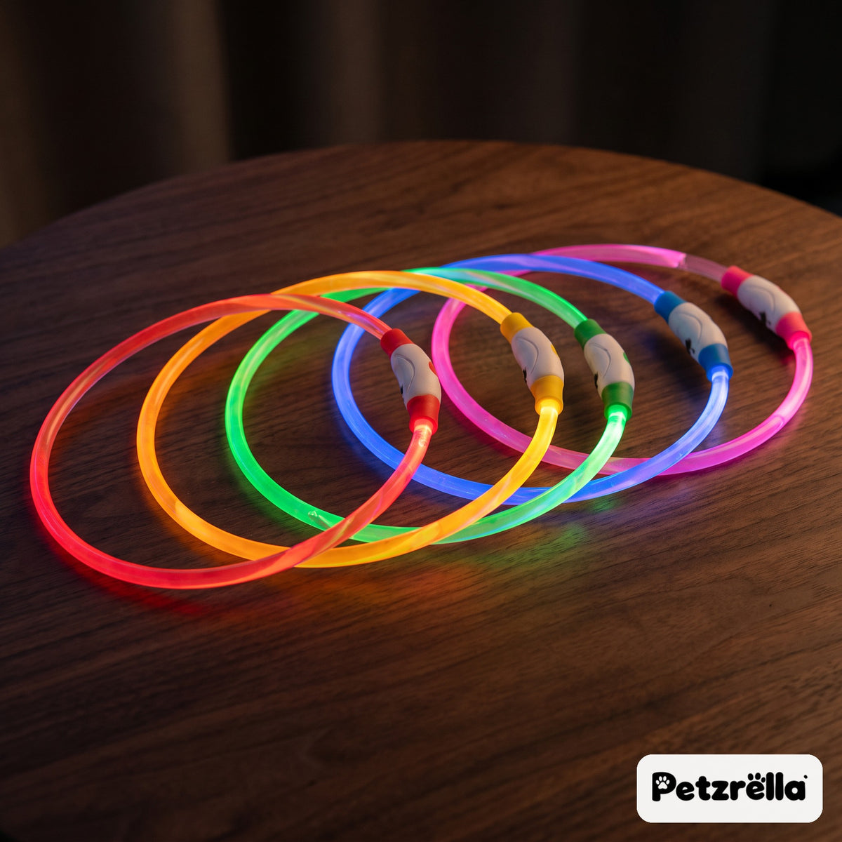 Petzrella USB rechargeable LED pet collars glowing in five colours on a wooden table
