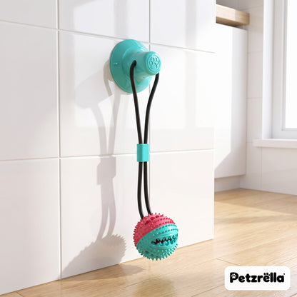 Petzrella suction tug toy in reddish blue with treat ball stuck to a kitchen tile wall